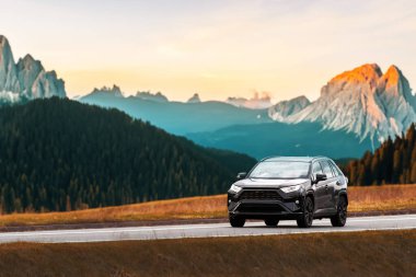 Modern aile arazi aracı görkemli bir doğa ve arka planda altın bir günbatımına sahip manzaralı bir yol boyunca seyahat eder. Daha fazla off-road kapasitesine ve 4WD 'ye sahip alt kompakt kamyon