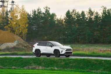 Modern ve lüks bir SUV, altın bir gün batımı gökyüzünün nefes kesici manzarasıyla asfalt bir yolda seyahat eder..