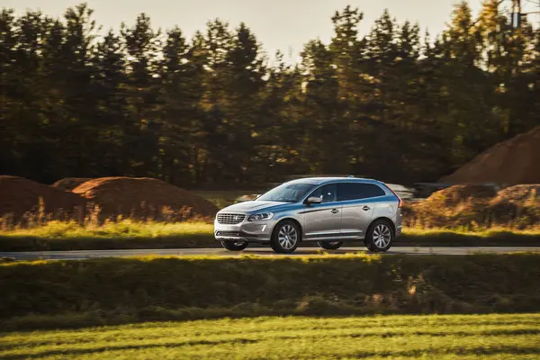 Melez bir SUV arabası görkemli bir doğa ve arka planda altın bir günbatımına sahip manzaralı bir yolda ilerliyor..