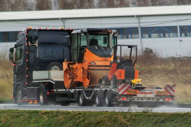 İnşaat malzemeleri nakliyesi. Kazı araçları ve vinçler otoyoldaki uzun römorklu nakliye kamyonunda..