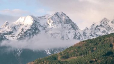4K yüksek kaliteli Alp dağları, güneş ışınları ve bulutlar karla kaplı kayalık tepeler üzerinde.