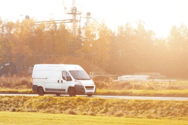 Teslimat minibüsü güneşli bir yol boyunca paketler taşır, tam zamanında hizmet ve müşteri memnuniyetini sağlar.