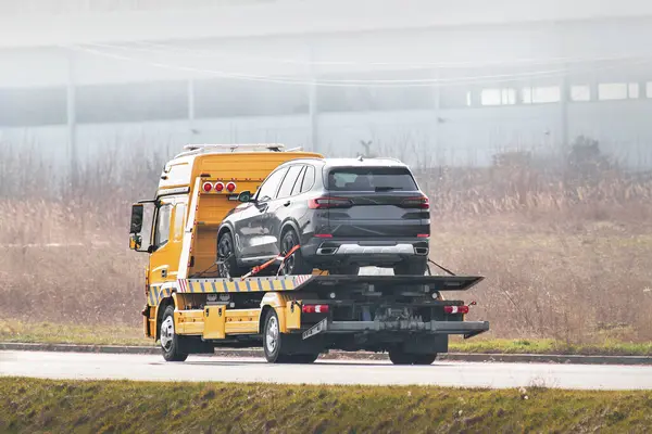 Flatbed towing truck with a car on the road. Roadside assistance. Car service transportation concept.