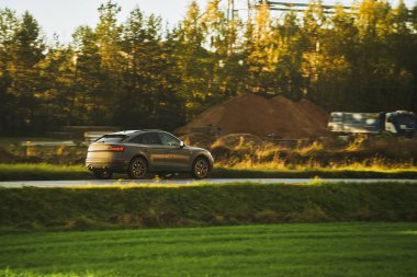 Alt kompakt bir SUV arabası arka planda muhteşem bir günbatımı ve dağlarla manzaralı kırsal bölgeleri keşfediyor..