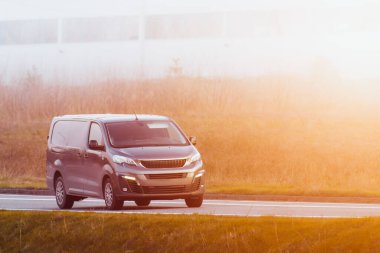 Teslimat minibüsü güneşli bir yol boyunca paketler taşır, tam zamanında hizmet ve müşteri memnuniyetini sağlar.