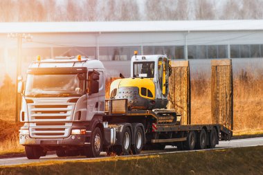 Flatbed Truck inşaat alanına ağır makineler getiriyor. Kazı makinesi ya da vinç. İnşaat endüstrisi.