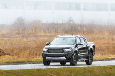 Banliyö yolunda sanayi zeminli siyah bir pikap.