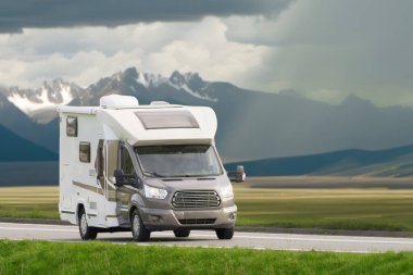 Karavan arka planda görkemli dağlarla bir otoyolda seyahat ediyor.