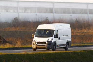 Beyaz minibüs manzaralı köy yolunda hızla ilerliyor.