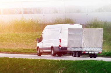 Karavanlı araba güneşli kırsal yolda.