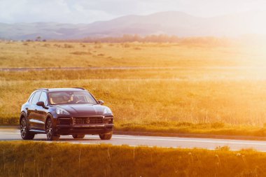 Kırsal yolda manzaralı ve yeşil arazili siyah bir SUV.