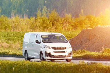 Beyaz minibüs yemyeşil tarlalardan geçiyor.