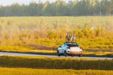 Kırsal yolda araba sürüyor, çatıda bisikletler var.