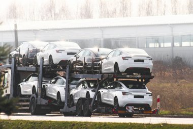 06.05.2024 Polonya, Avrupa. Endüstriyel binaların önünden geçen yeni Tesla elektrikli arabaları getiren bir kamyon.