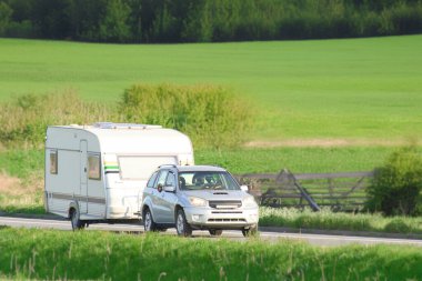 Yolda araba ve karavanla seyahat sahnesi.