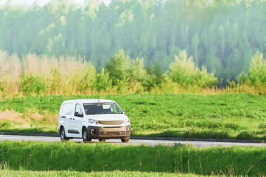 Kırsal yolda beyaz minibüs sürüyor.