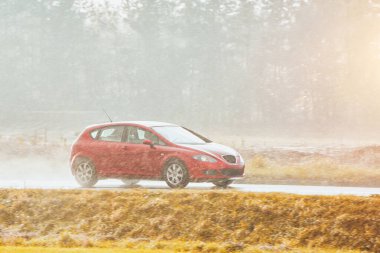 Kaygan yolda yağmurun içinden geçen küçük bir araba