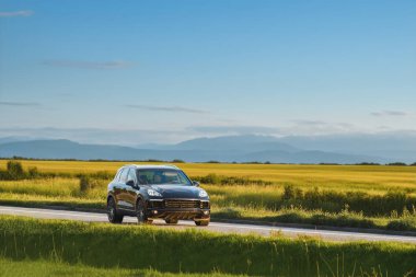 Modern siyah SUV gün batımında bir kır yolunda geziniyor.