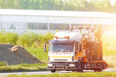 Yaz boyunca kırsal bir yolda mini kazıcı taşıyan bir çekici.