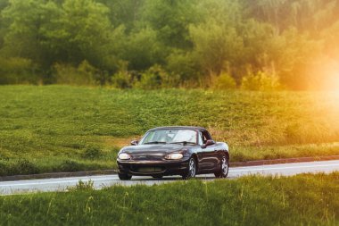 Klasik Japon roadster gün batımında manzaralı köy yolunda gidiyor.