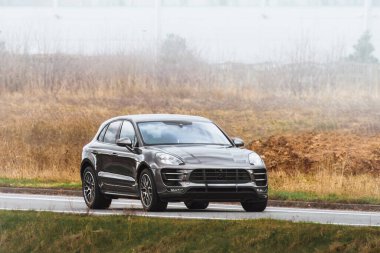 Siyah lüks SUV dağlarla dolu manzaralı kırsal alanda ilerliyor.