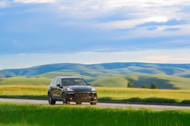 Siyah lüks Alman SUV gün batımında kır yolunda gidiyor.