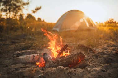 Glowing campfire and tent under the evening sky clipart