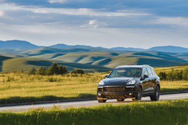 Siyah SUV gün batımında bir ülkede geziniyor.