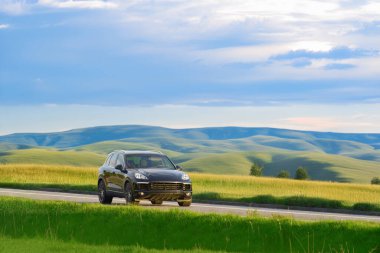 Şatafatlı siyah SUV gün batımında bir kır yolunda sürüyor.