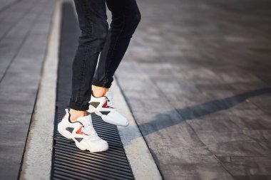 Beyaz spor ayakkabı ve siyah kot giyen adam kaldırımda dikiliyor.