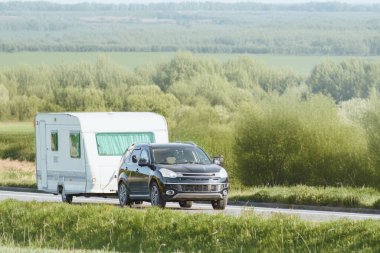 Araç yeşil arazide karavan taşıyor.