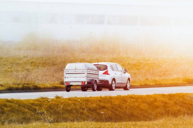 Karavanı olan beyaz bir araba kırsal bir yolda ilerliyor.