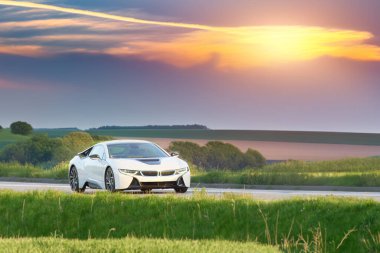 Beyaz araba yaz güneşinde yeşil araziyi geçiyor.