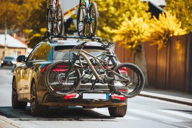 Car is driving through a sunny urban area with bicycles securely mounted on a rack.