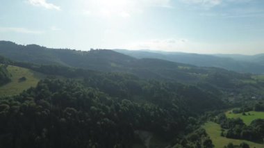 Açık mavi gökyüzü ve bulutları olan ormanlık dağların manzaralı manzarası.
