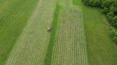 Kırmızı traktörün hava görüntüsü çimenlik alanı kesiyor