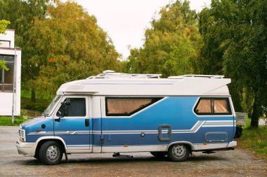 Beyaz karavan ağaçlarla dolu bir yere park edilmiş.