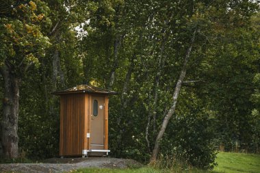 Ağaçlarla çevrili küçük ahşap tuvalet.