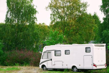 Manzaralı bir alanda ağaçların yanına park edilmiş beyaz bir karavan.