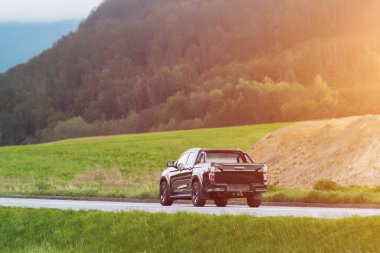 Kırsal alanda siyah bir kamyonet sürüyor.