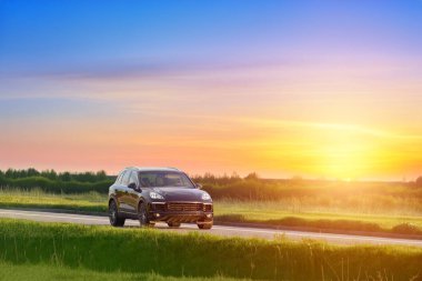 Gün batımında şehir yolunda siyah lüks SUV.