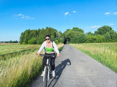 Kadın bisikletçi kırsal yolda güneşli bir günün tadını çıkarıyor