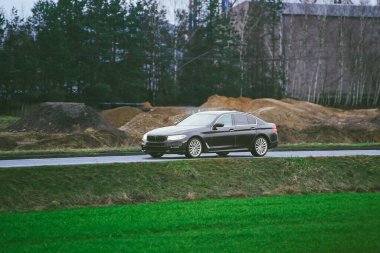 Performance sedan driving by forest area clipart