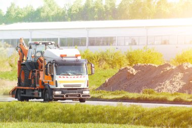 Yaz günü kırsal yolda kazıcı taşıyan bir çekici.