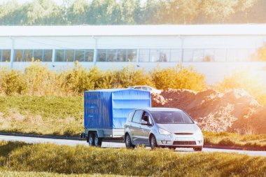 Araba ve karavan güneşli bir yolda ilerliyor.