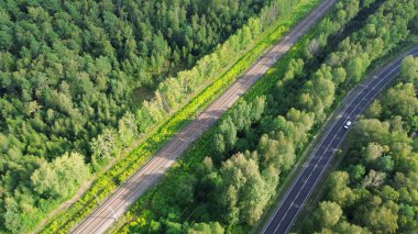 Yeşil bir ormandan geçen demiryolu ve yol manzarası