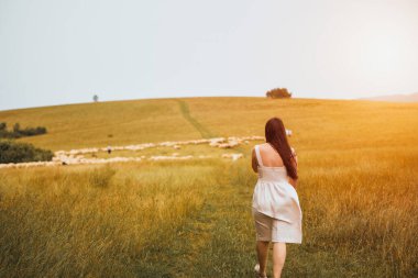 Yeşil tarlada dolaşan bir kadın otlayan koyunlarla çevrili.
