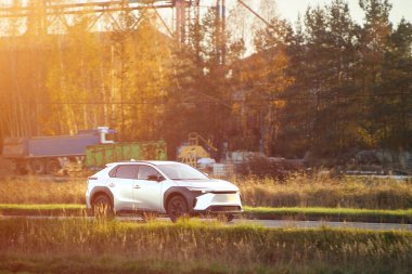 Sonbahar ağaçlarının yanından geçen beyaz hibrit araç.