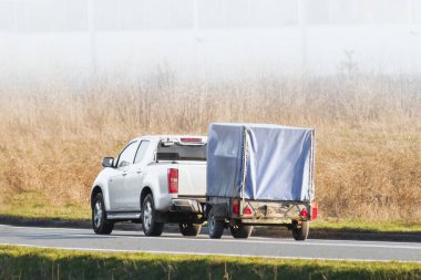 White car towing trailer on sunny rural road clipart