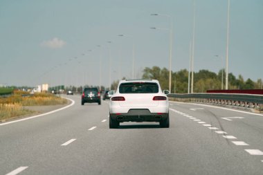 Beyaz araba açık bir yolda ilerliyor..